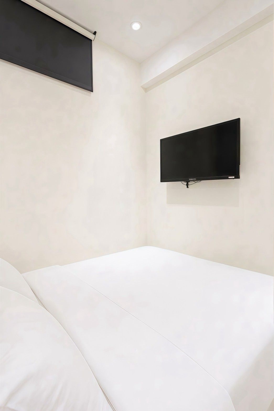A room with a bed, a mounted TV, and a ceiling light.