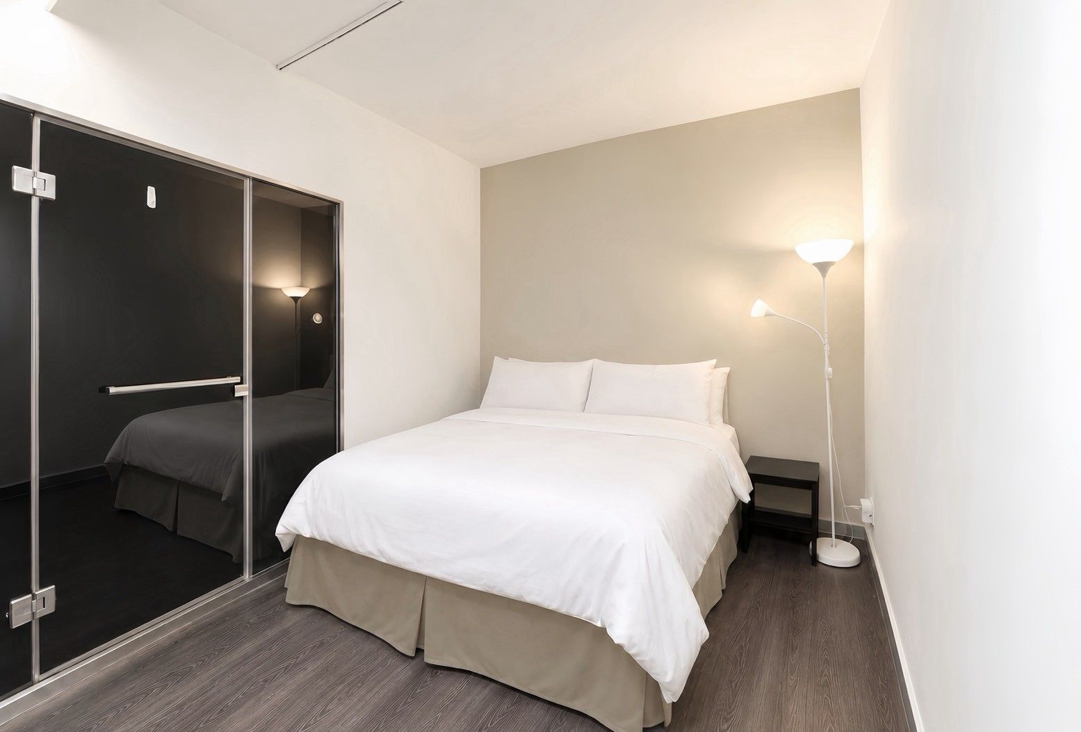 A modern hotel room with a bed, a bedside table, a lamp, and a sliding door leading to a bathroom.