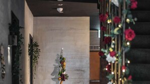 Ein Flur mit einer Betonwand, einer hängenden Obstdekoration und einer Treppe mit roten Blumen und Lichtern.