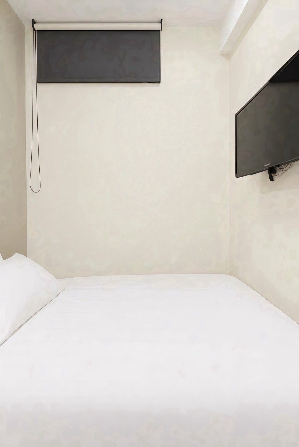 Een minimalistisch hotelkamer met een bed, een wandtelevisie en een plafondlamp.