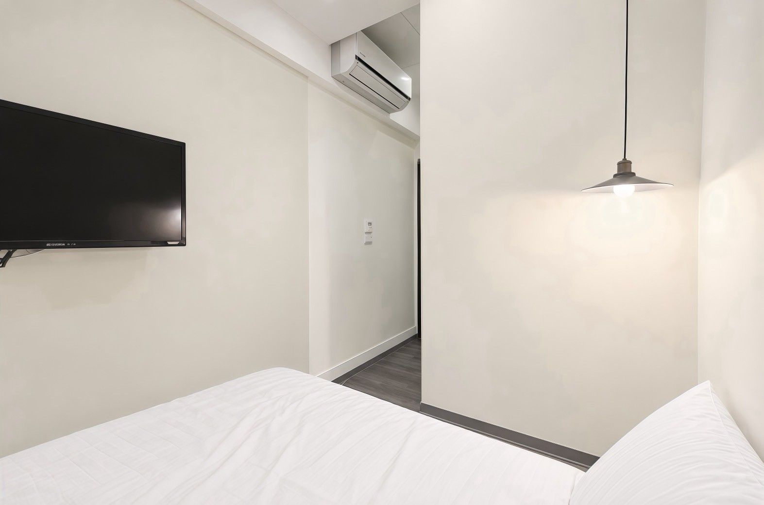 Una habitación de hotel moderna con una televisión de pantalla plana montada en la pared, una lámpara colgante y una cama bien hecha.