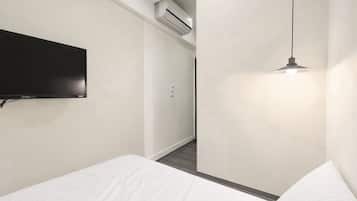 Una habitación de hotel moderna con una televisión de pantalla plana montada en la pared, una lámpara colgante y una cama bien hecha.