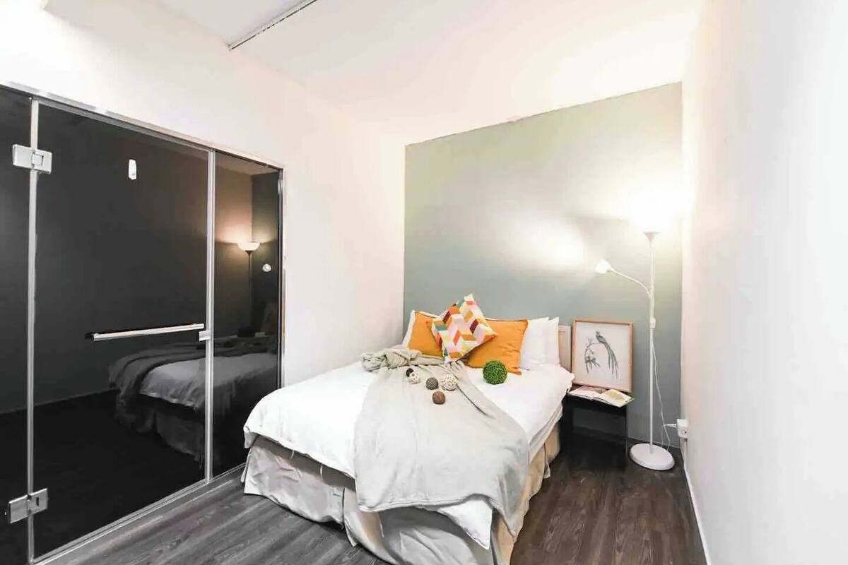A modern hotel room with a bed, bedside table, lamp, and a large mirror.