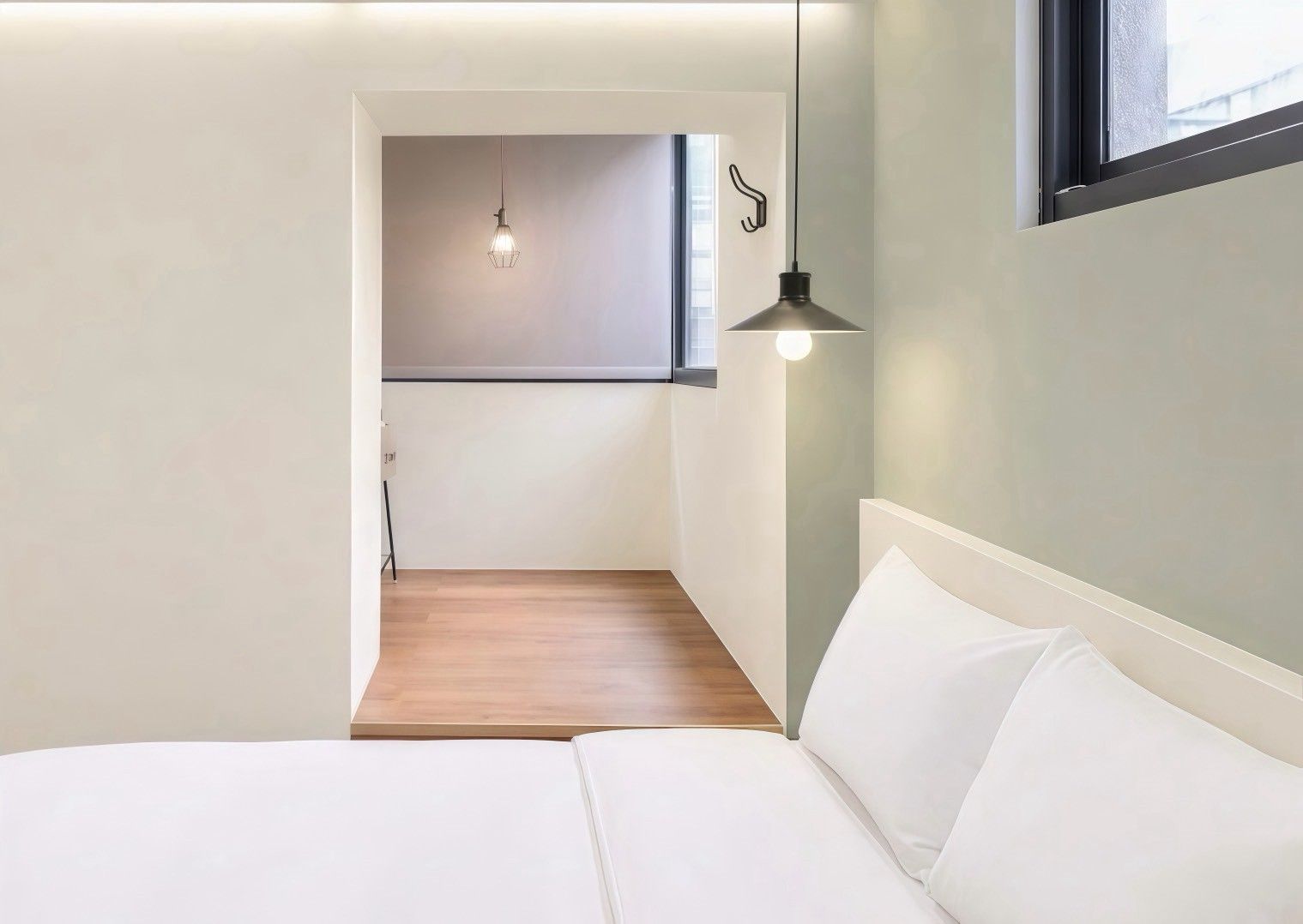 A minimalist bedroom with a bed, a hanging light fixture, and a window.