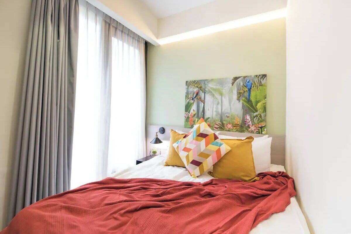 A hotel room with a bed, a painting on the wall, and a window with curtains.