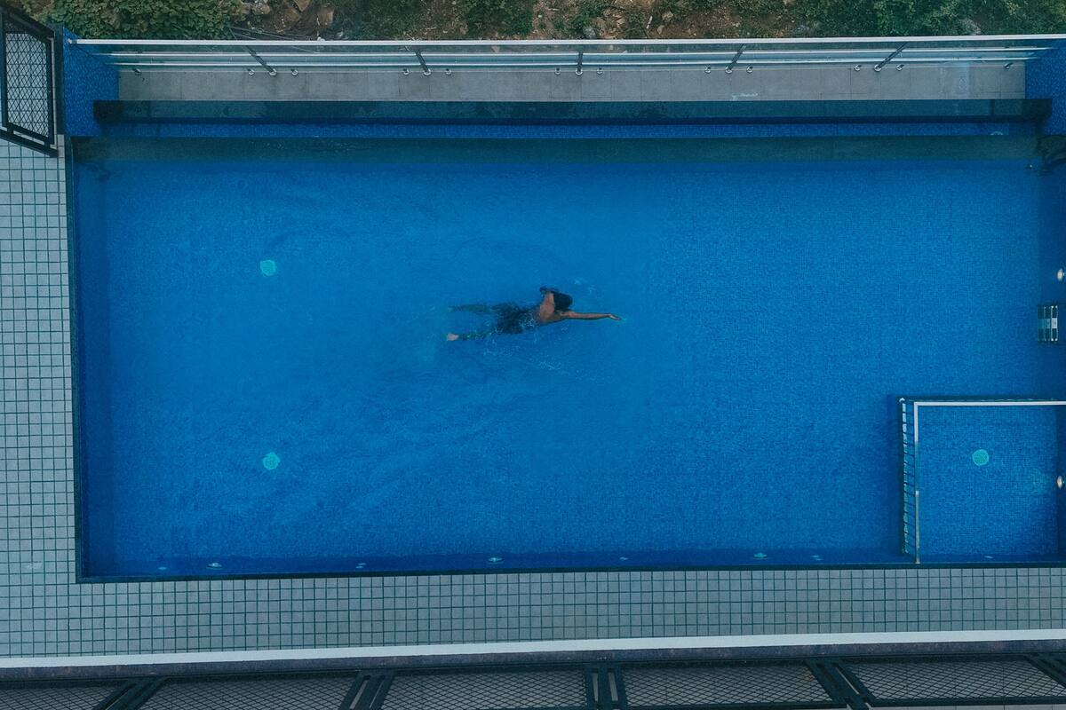 Una vista aerea di una piscina rettangolare con un solarium piastrellato tutt'intorno.