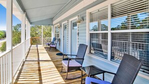 Une véranda couverte avec un plancher en bois, des balustrades blanches et une rangée de chaises.
