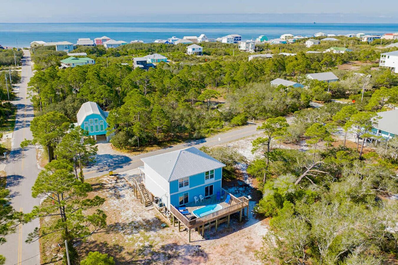 A coastal property with a large house featuring a swimming pool, surrounded by dense greenery and a clear view of the ocean.