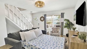 A modern bedroom with a grey sofa, a bed with a blue and white patterned bedspread, a wooden desk with a TV, and a staircase. - Sleeps 16 · Private Pool · 3 Blocks to Beach (Gulf Shores)
