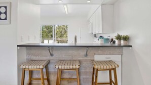 A modern kitchen with a white countertop, three wooden stools, and a view of the outdoors through a window. - Sleeps 16 · Private Pool · 3 Blocks to Beach (Gulf Shores)