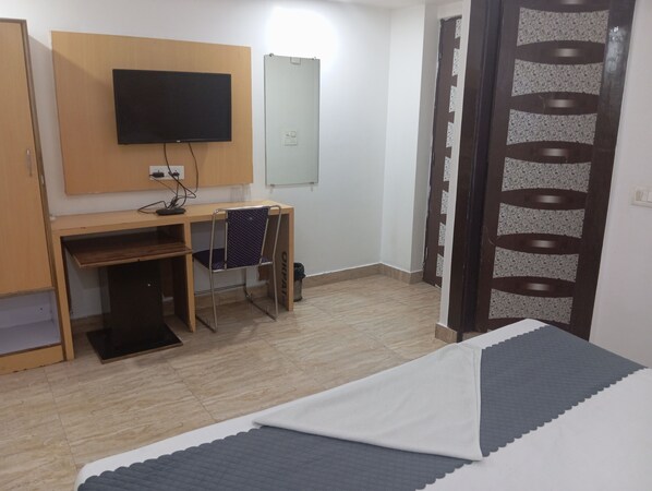 A hotel room with a bed, a desk with a chair, a TV mounted on the wall, and a door with a patterned design. - Hotel Future Inn (Noida)