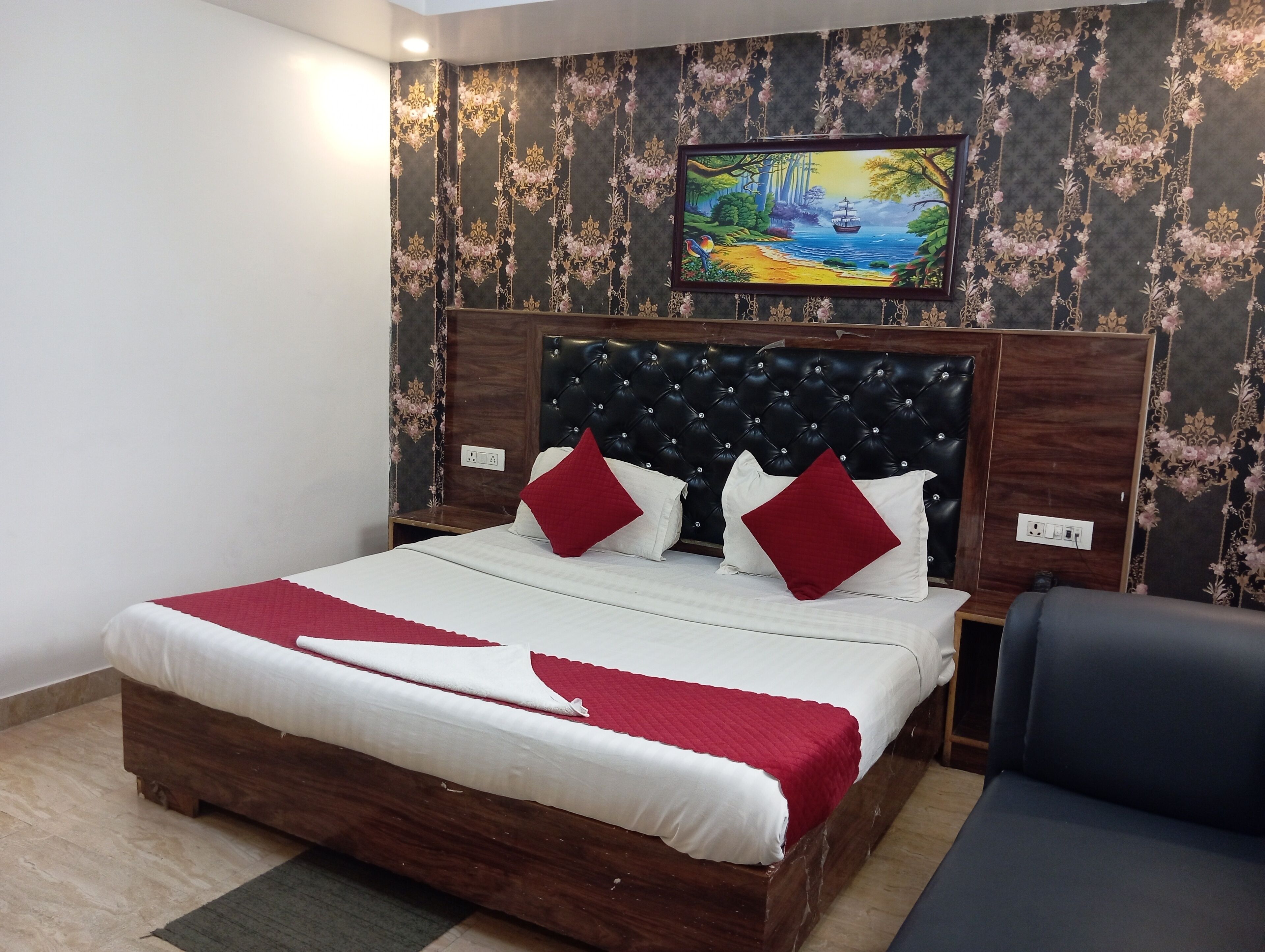 A bedroom with a wooden bed, red and white bedding, a black headboard, and a floral wallpaper.