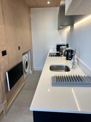 A modern kitchen with a built-in washing machine, a coffee machine, and a sink. - Manchester - Sky Garden - 2 Beds - Sleeps 4 (Manchester)