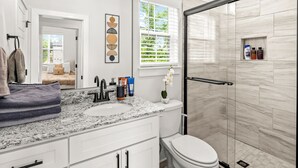 Ein modernes Badezimmer mit einer Granittheke, einer weißen Toilette und einer Duschkabine aus Glas.