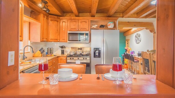 A wooden kitchen with a dining table set for two, featuring a microwave, refrigerator, and stove. - Beautiful and fun 5 bedroom house with a hot tub, arcade games and lots of room. (Albuquerque)