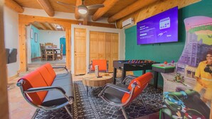 A room with a foosball table, two orange chairs, a wooden ceiling, and a television displaying a game. - Beautiful and fun 5 bedroom house with a hot tub, arcade games and lots of room. (Albuquerque)