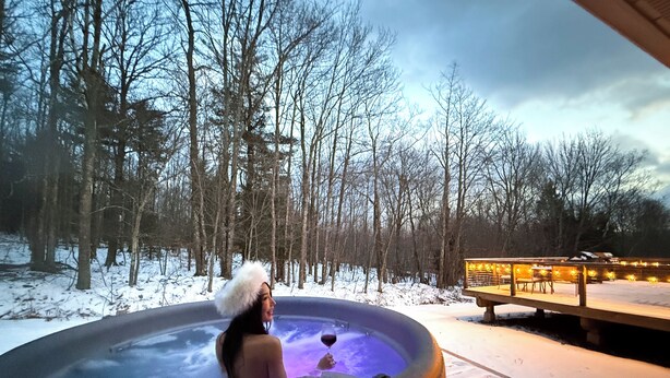 A hot tub in a snowy outdoor setting with a wooden deck and a bench.