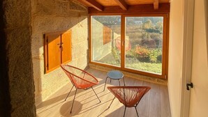 Ein Zimmer mit Steinwand, Holzbalkendecke, zwei Fenstern und zwei roten Stühlen.