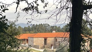 Ein Steingebäude mit rotem Ziegeldach, umgeben von Bäumen und einem Bergpanorama.