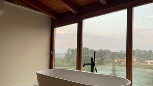 Ein modernes Badezimmer mit freistehender Badewanne, großen Fenstern und Blick auf eine grüne Landschaft.