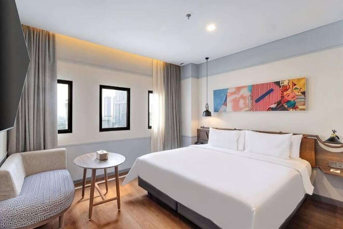 A hotel room with a large bed, a small round table, a chair, and a painting on the wall.