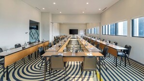 Een vergaderruimte met een lange tafel, meerdere stoelen en een groot scherm aan de voorzijde.