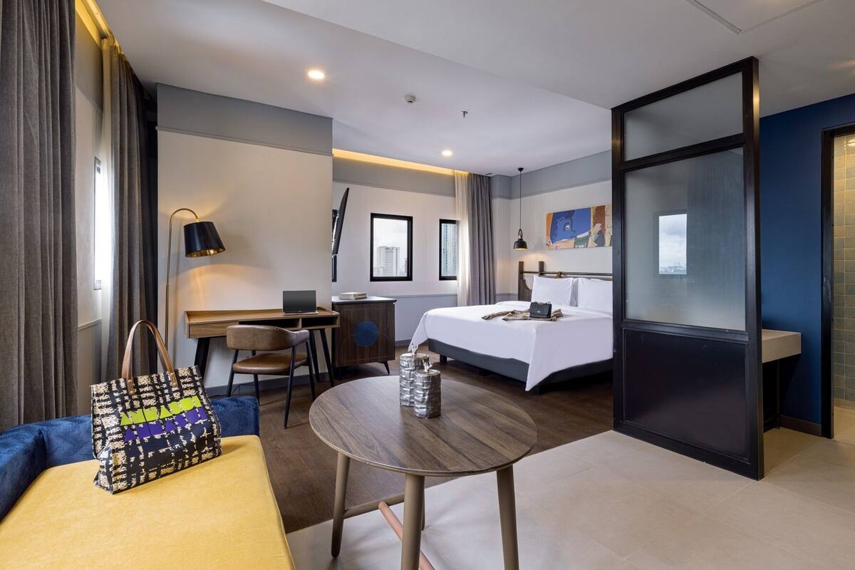 A modern hotel room with a bed, desk, and seating area.