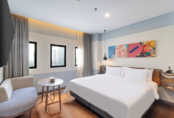 Une chambre d’hôtel avec un grand lit, une chaise, une petite table et un tableau au mur.