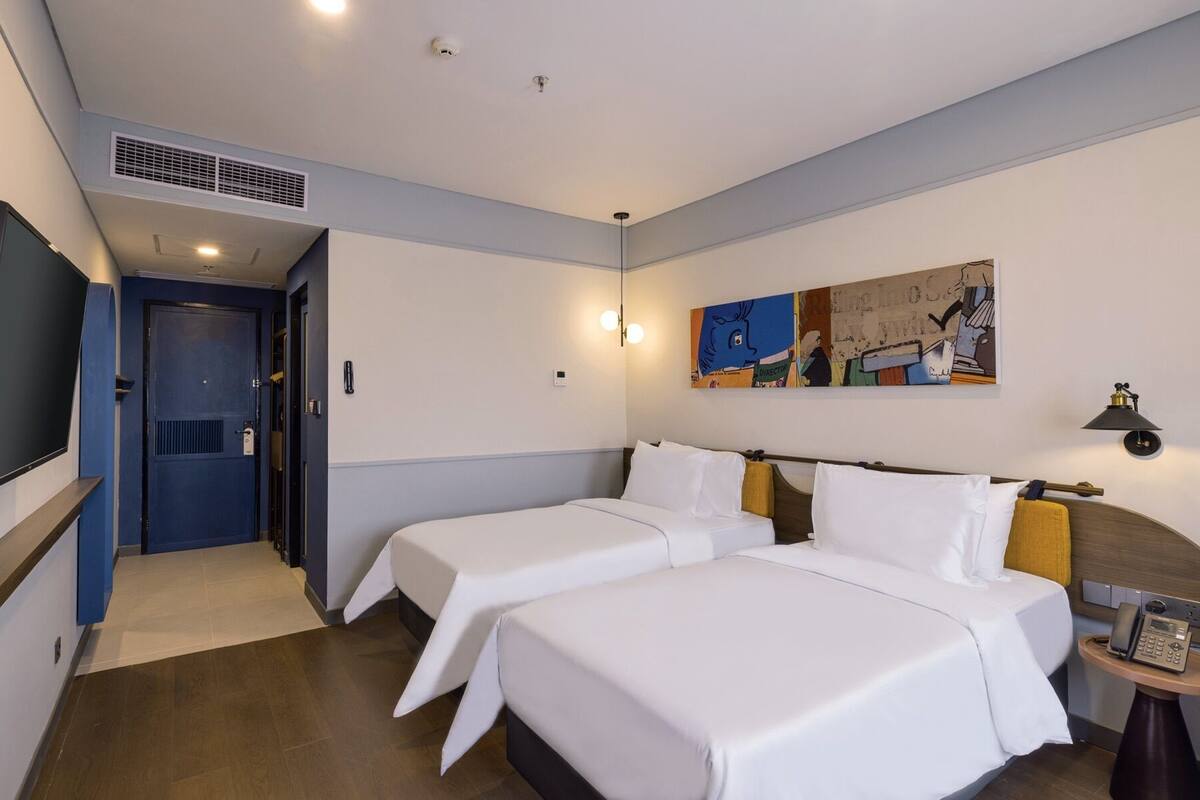 A hotel room with two beds, a TV, a painting, and a phone on a bedside table.