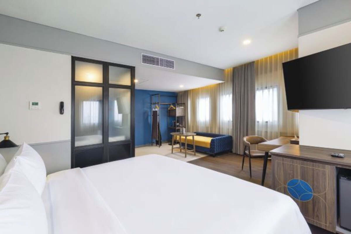 A hotel room with a large bed, a desk with a chair, a TV mounted on the wall, and a wardrobe with a mirror.
