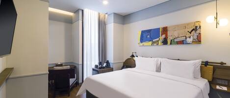 Habitación de hotel con una cama grande, un escritorio, una silla, un televisor de pantalla plana, un cuadro en la pared y una ventana con cortinas.