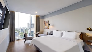 Een hotelkamer met een groot bed, een bureau, een stoel en een uitzicht op de stad door grote ramen.