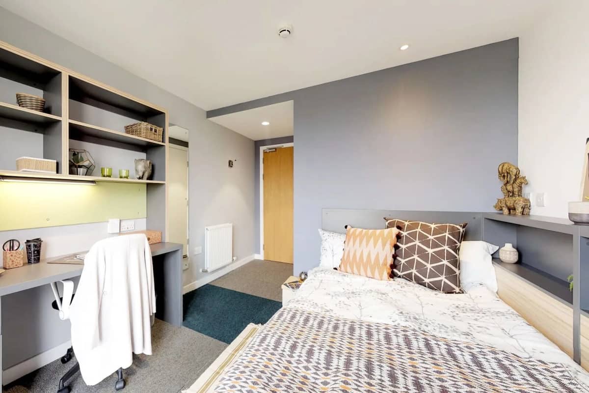 A modern hotel room with a bed, a desk, and shelving.