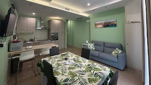 Ein kompakter Wohnraum mit Küchenzeile, einem Essbereich mit Tisch, einer Couch und einem Einzelbett.
