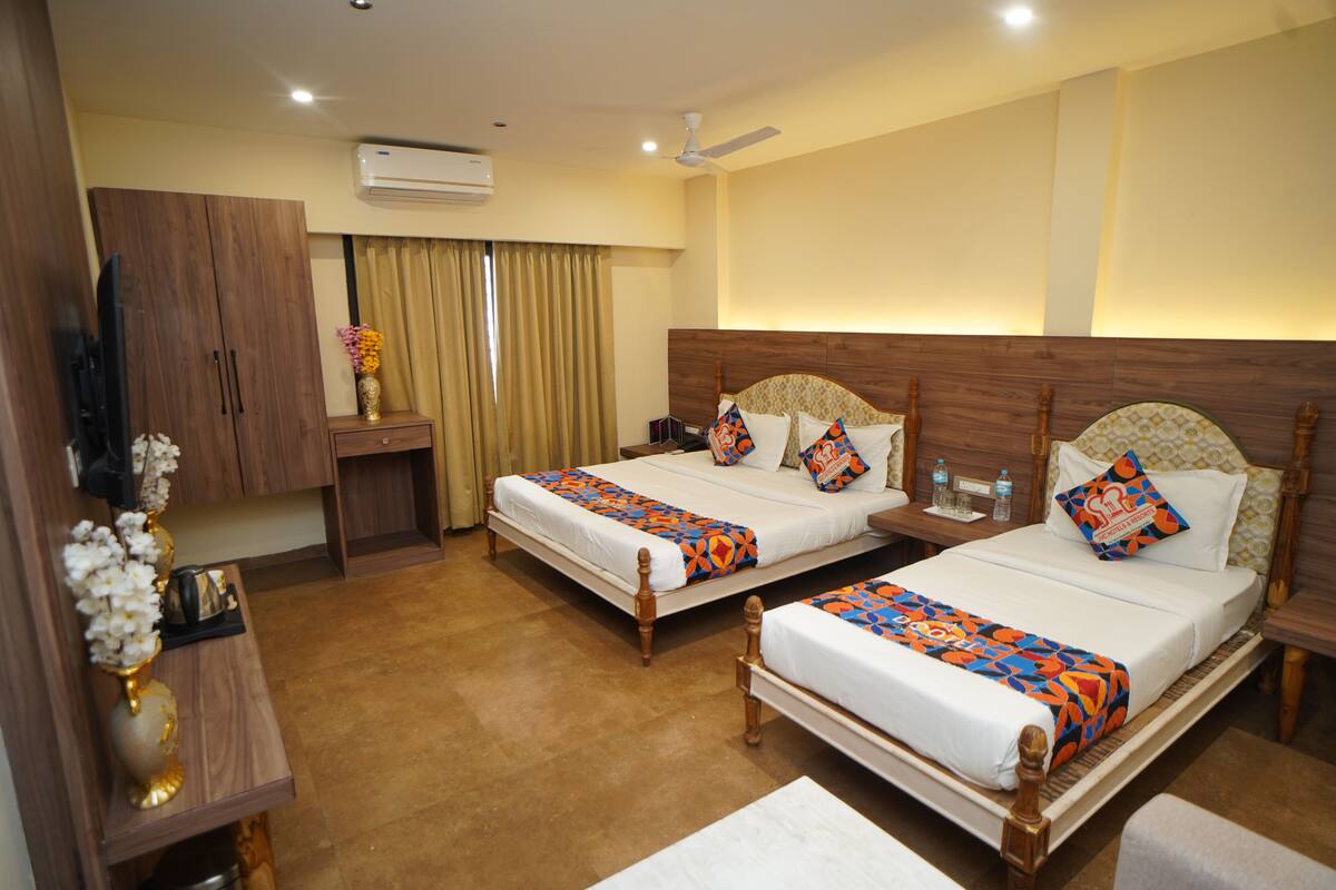 A hotel room with two beds, a TV, an air conditioner, and a ceiling fan.