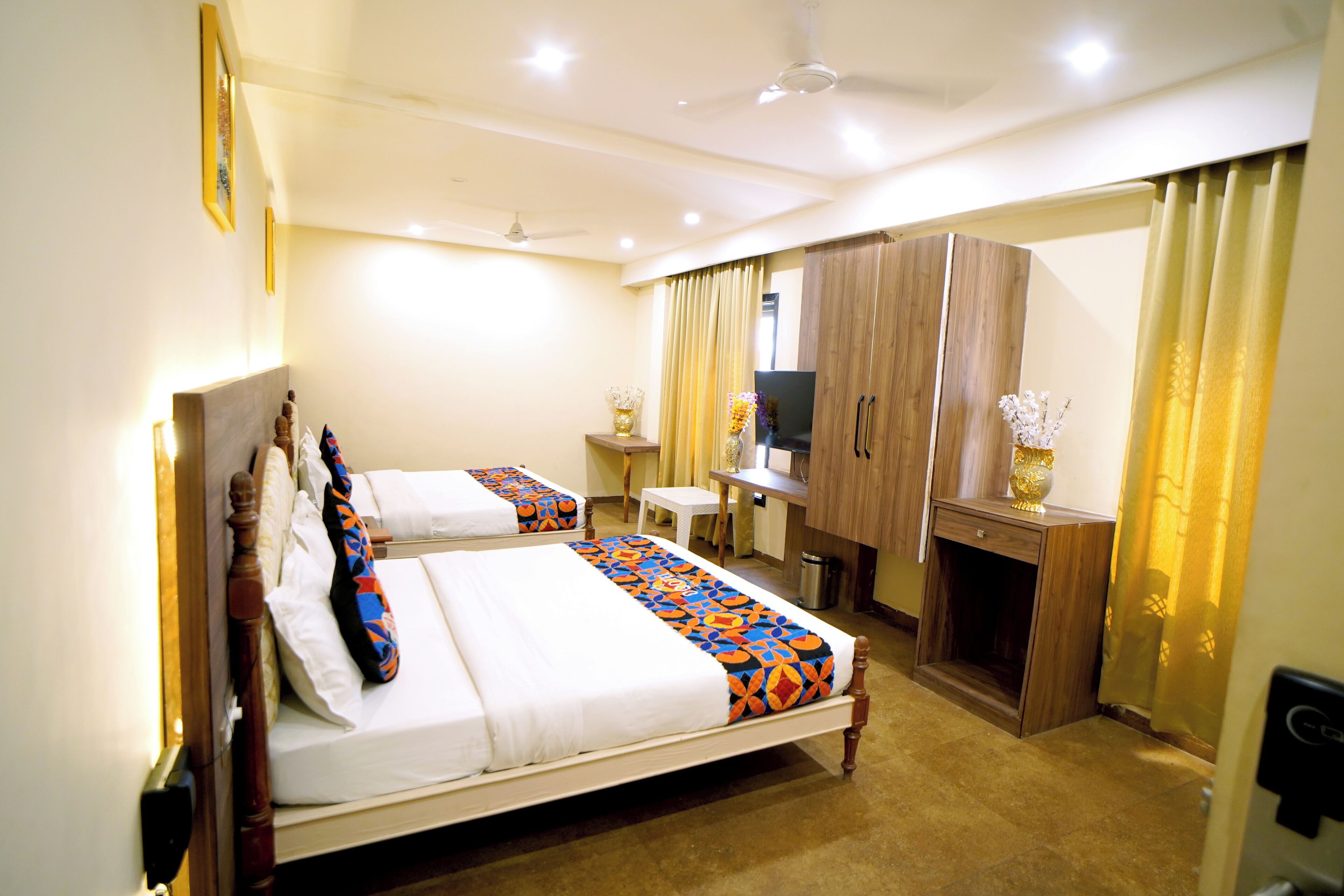 A hotel room with two beds, a desk, a wardrobe, and a small seating area.