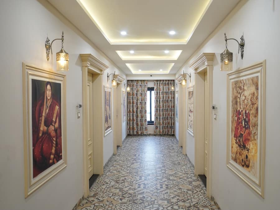 Un pasillo con baldosas de diseño, obras de arte colgadas en la pared, iluminación empotrada en el techo y vista a una habitación con cortinas estampadas.