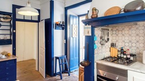 A kitchen with a gas stove, shelves with kitchenware, and a blue door. - Central Ericeira Apartment with Lift (Ericeira)