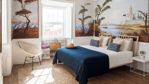 A bedroom with a bed, a chair, a nightstand, and a mural on the wall. - Central Ericeira Apartment with Lift (Ericeira)