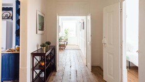 A hallway with a wooden floor, a dark wooden console table with decorative items, and a white door on the right. - Central Ericeira Apartment with Lift (Ericeira)