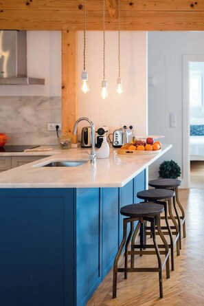 A modern kitchen with a central island, bar stools, hanging light fixtures, and a variety of kitchen appliances.