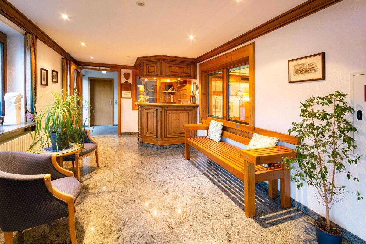 A hotel lobby with a wooden bench, a small table, and chairs. There is a potted plant and a framed picture on the wall.