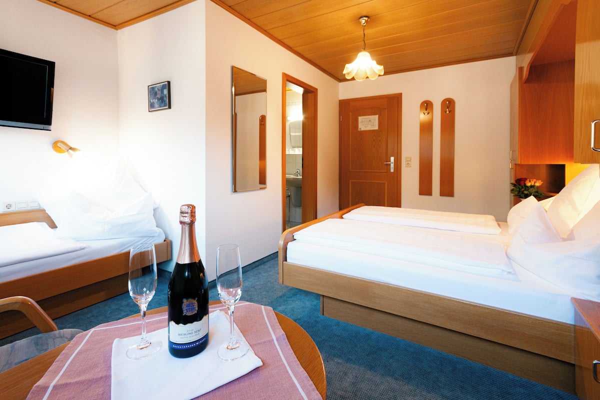 A hotel room with two beds, a TV, a bottle of champagne, and a glass on a table.