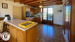 A kitchen with wooden cabinets, a central island, and a large window. - Charming cottage for 6 in Jard-sur-Mer, close to beach and Vélodyssée (Jard-sur-Mer)