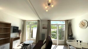 Ein geräumiges Wohnzimmer mit Sofa, Fernseher, Esstisch und großem Fenster.