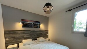 Ein Schlafzimmer mit einem Bett, Nachttischen, einer Wandleuchte, einem Fenster und einem Gemälde.