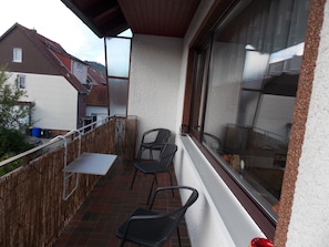 A balcony with a table and two chairs, a window with a view of the neighborhood, and a wooden fence. - Sehr Ruhige Ferienwohnung im 1. OG (Langelsheim)
