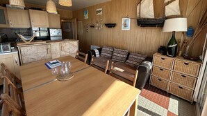 A cozy cabin-style kitchen with wooden cabinets, a dining table, and a sofa. There are wicker baskets and a lamp on the counter. - 3-room flat with balcony, sleeps 6 in Saint-Jean-de-Monts (Saint-Jean-de-Monts)