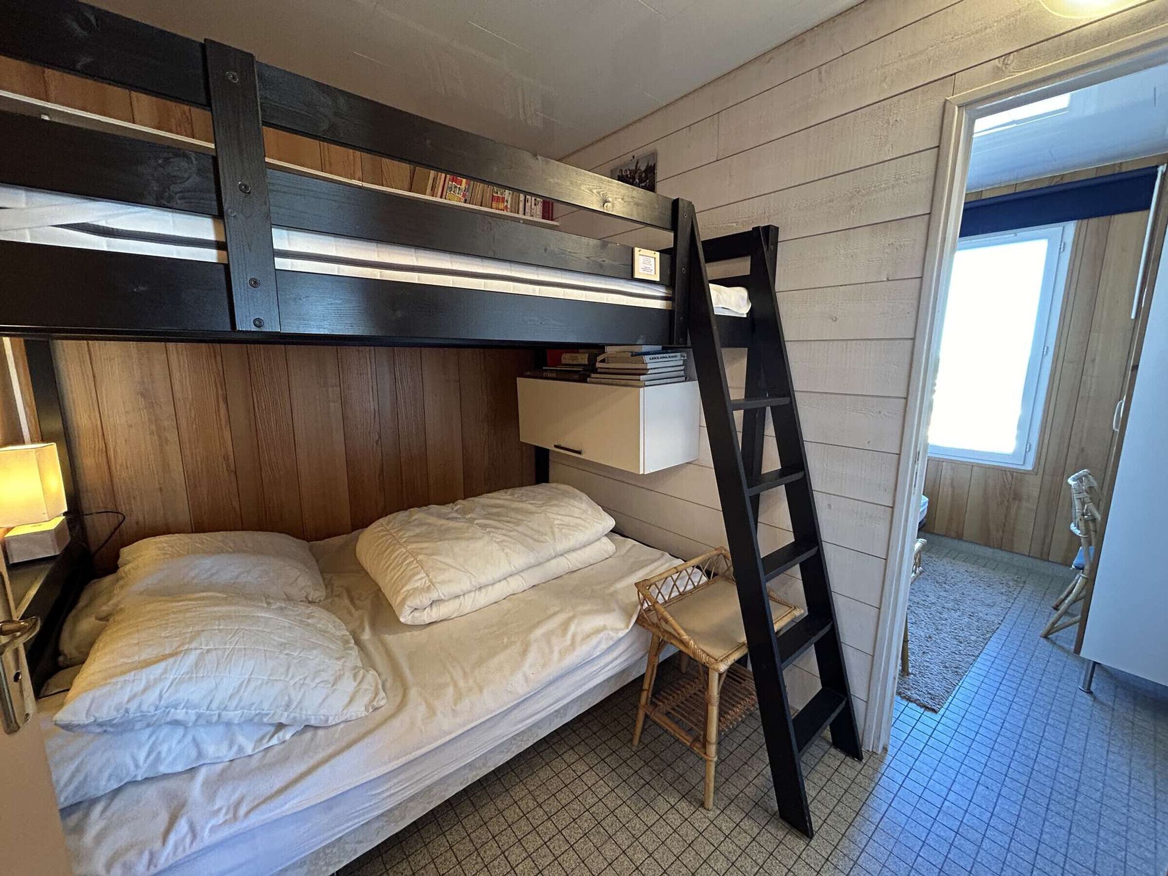 A bunk bed with a ladder, a small chair, and a shelf above the bed.