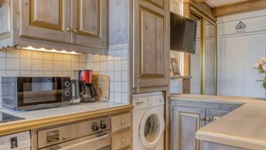 A kitchen with wooden cabinets, a microwave, a coffee maker, a washing machine, and a TV. - Central Megève Apartment - 4 Guests - Pets Allowed (Megève)